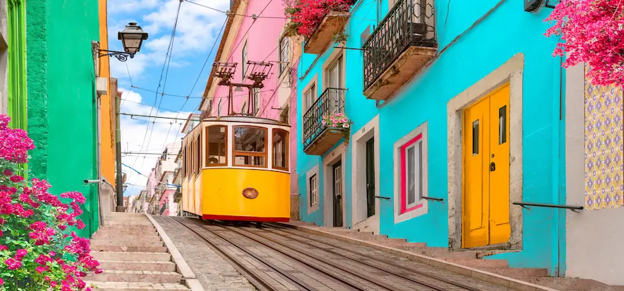 Tramvai galben pe Rua da Bica cu case colorate și bougainvillea, Lisabona Portugalia - bilete avion