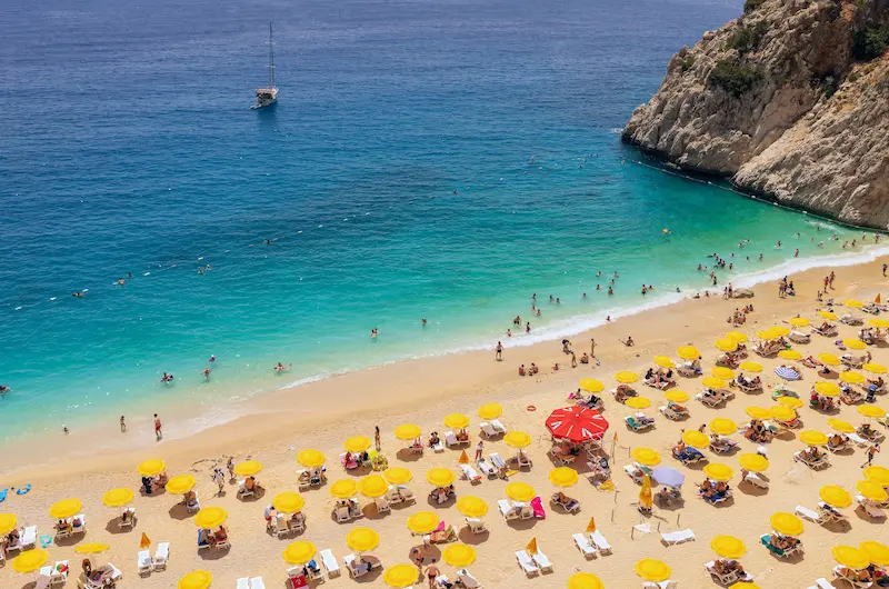 Plaja Kaputas din apropierea Kas, Antalya — umbrele galbene pe nisip și golf turcoaz, sejur charter Turcia