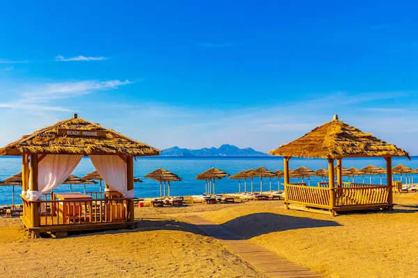 Cabane pe plajă din Kos cu șezlonguri, umbrele de paie și mare albastră — sejur charter Grecia, Dodecanez