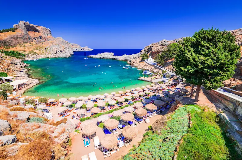 Golful Sfântul Pavel din Lindos, Rhodos — plajă cu umbrele de paie și acropola pe stâncă, sejur charter Grecia