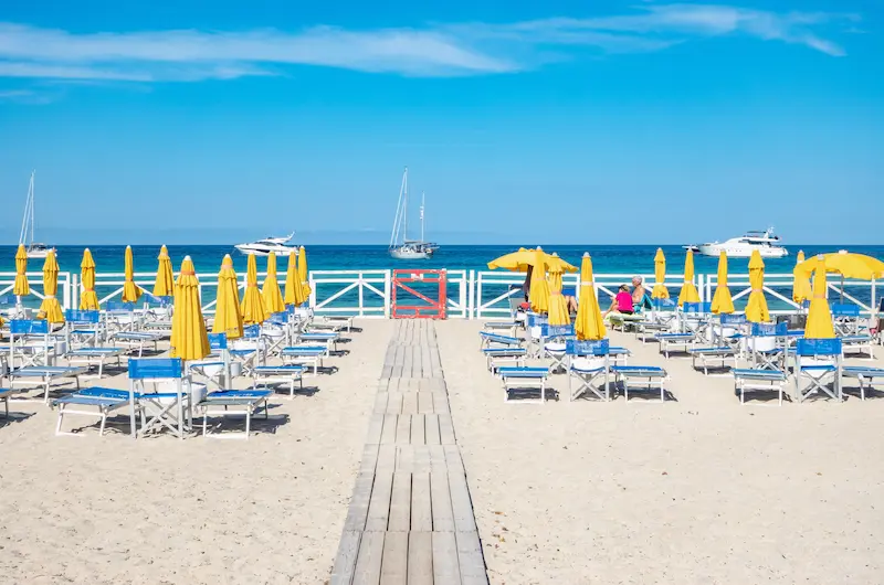 Plajă amenajată din Sicilia cu șezlonguri, umbrele galbene și iahturi la orizont — sejur charter Italia all-inclusive